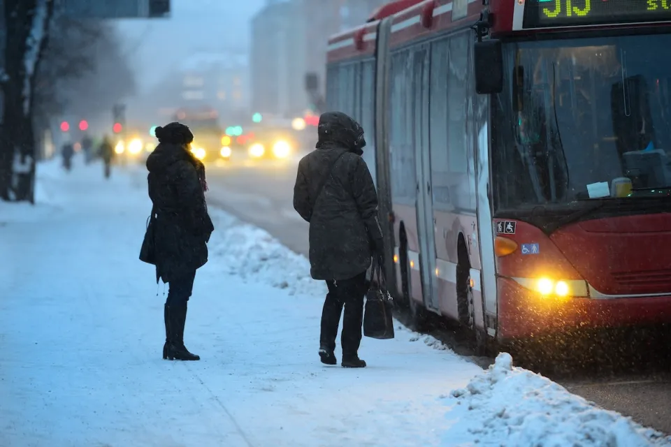Two people waiting to board arriving bus on a snowy day.